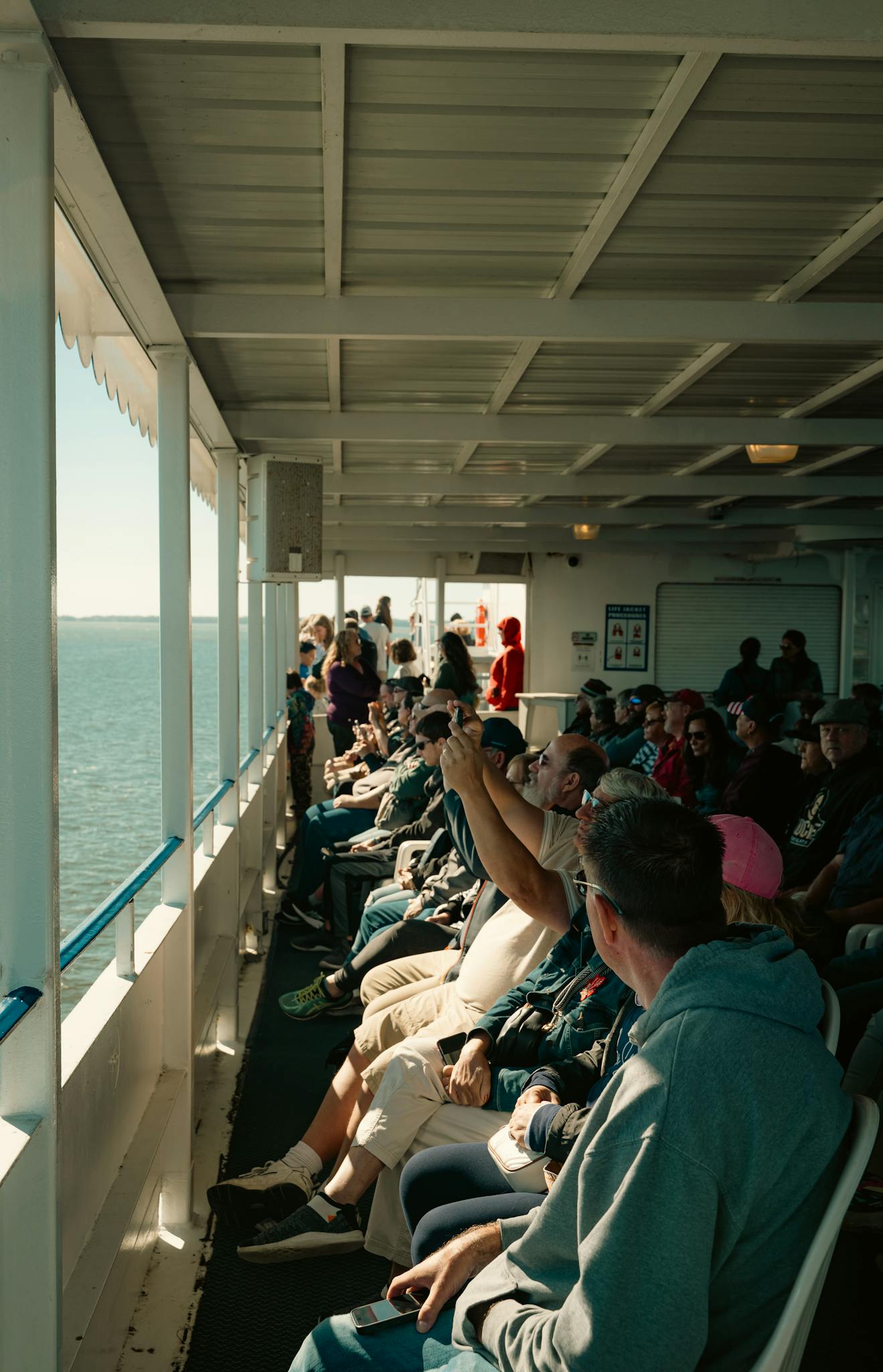 A diverse group of tourists enjoying a scenic ferry ride on a sunny day, capturing memorable moments.