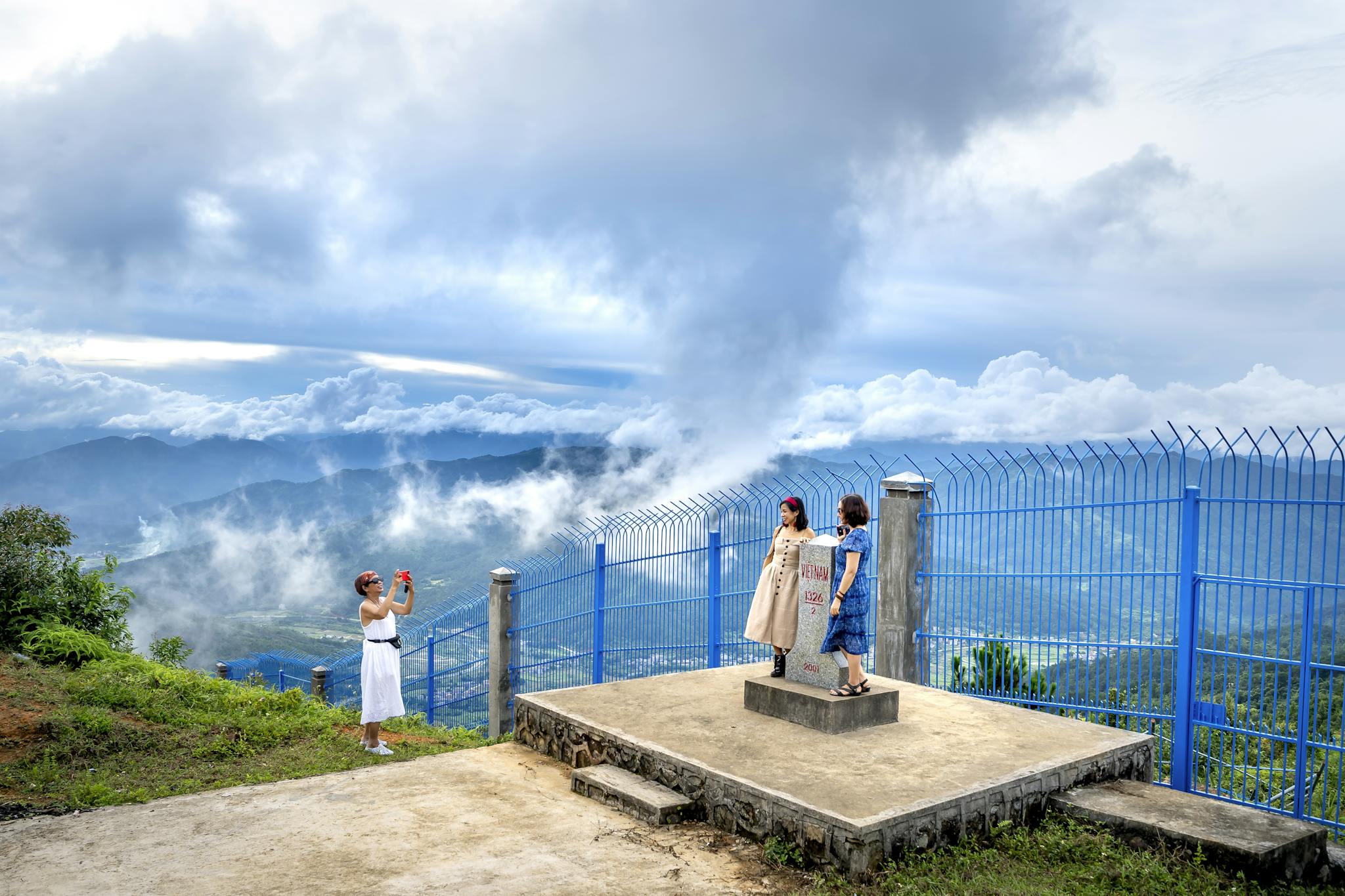 Three travelers capturing memories on a mountain vista with clouds and fog.